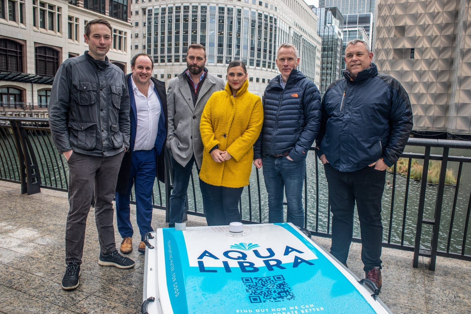 Six people standing on a London dockside behind an Aqualibra branded WasteShark drone.