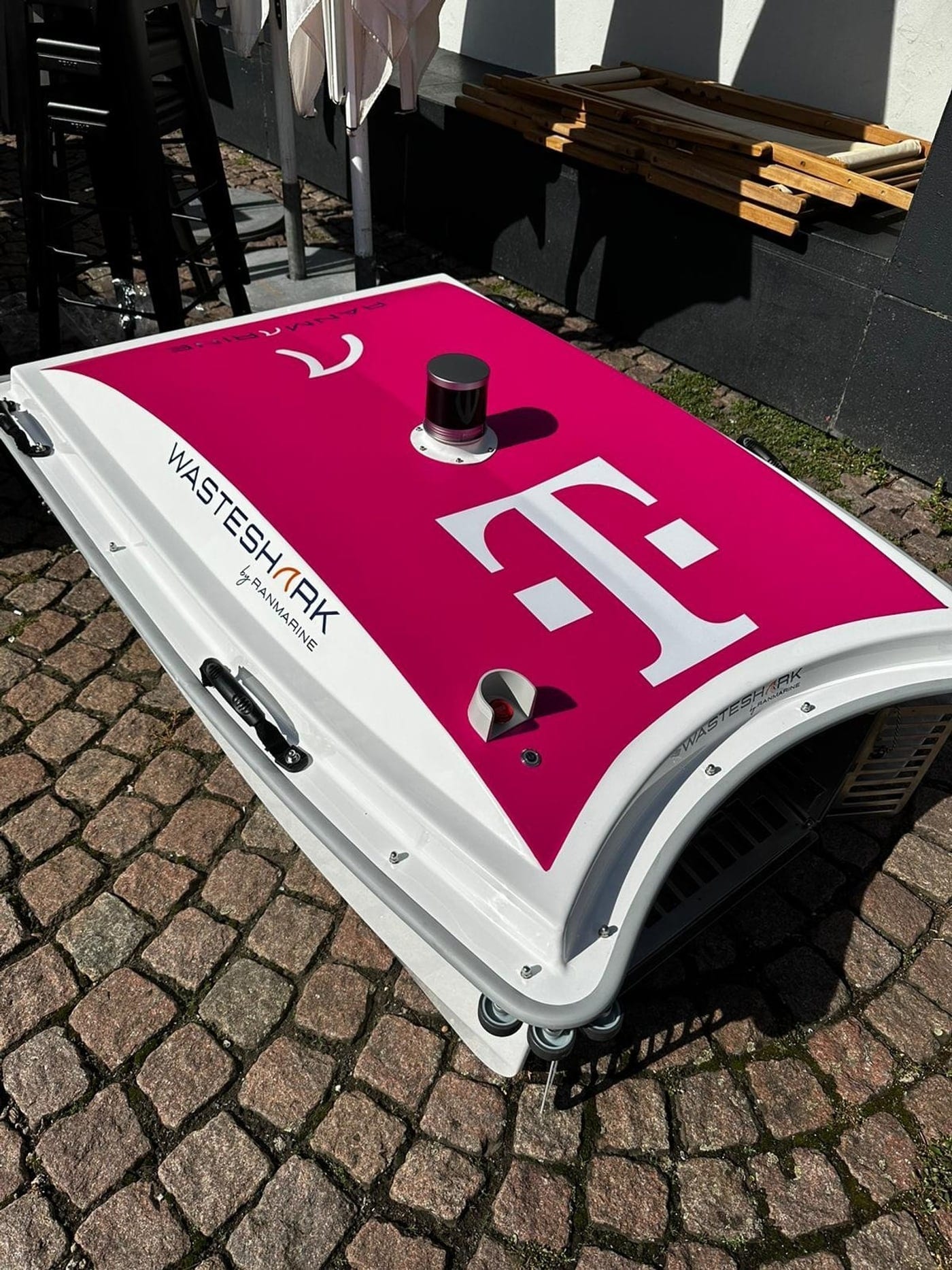 A T-Mobile branded WasteShark drone on a cobbled dockside, its magenta livery and logo facing the camera.