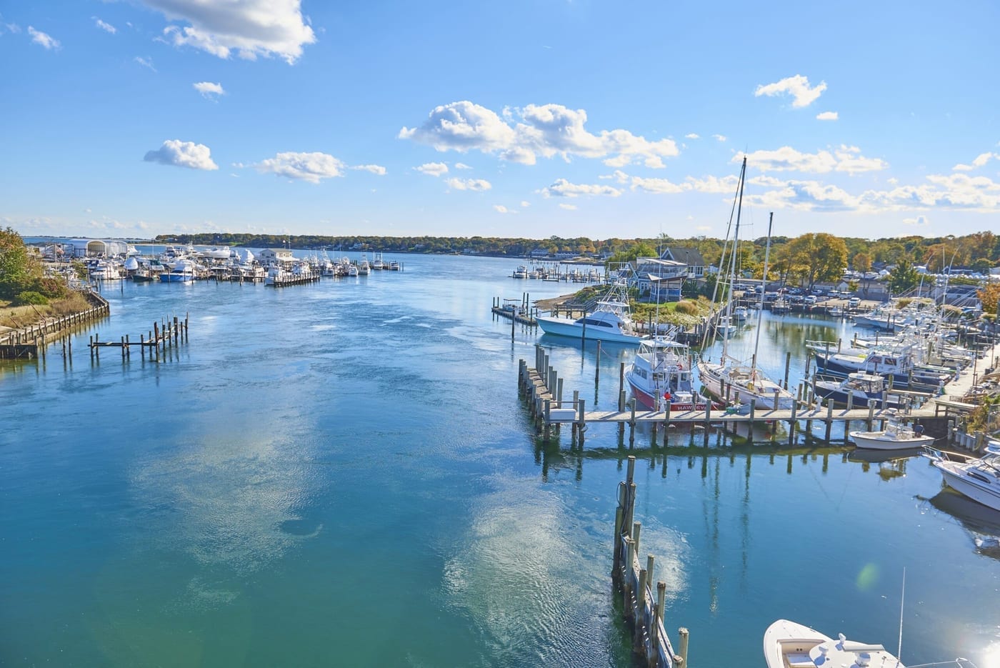 A Long Island inlet lined with moored boats and timber pilings under a blue sky.